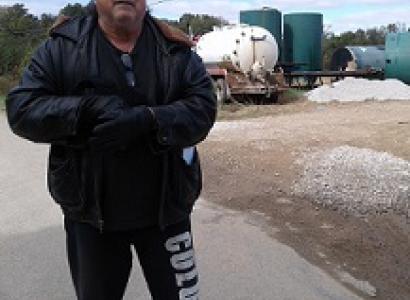 White man in winter coat standing in front of metal tanks and a truck