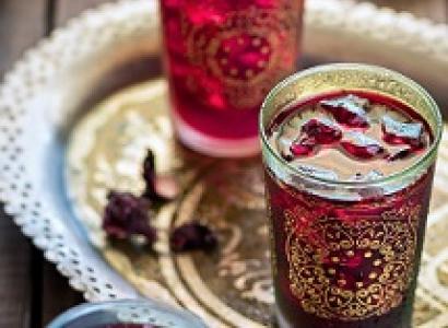 Two glasses with gold designs on the outside and red liquid inside on a pretty gold flouted tray against a wooden tabletop