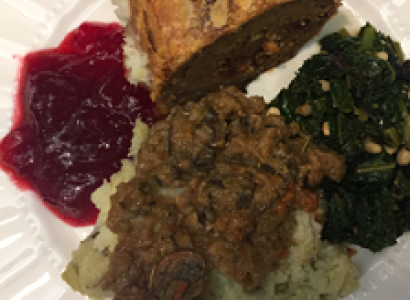 Top down view of a white plate with red cranberry sauce, a brown skinned potato something green and leafy on the side and what looks like rice with something brown on top
