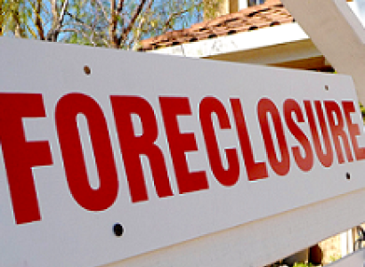 White sign with red letters saying Forclosure in front of a house