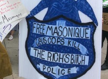 Woman holding a huge sign with a police badge that says Free Masonique Cbus Cops Kill 