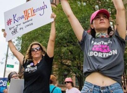 Two white women holding pro-choice signs above their heads looking very determined outside at a rally
