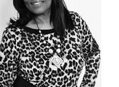 Black and white photo of a black woman with shoulder length hair, black rimmed glasses, a leopard print top and a necklace