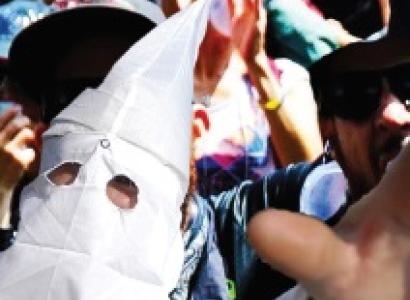 Klan member in pointy white mask holding his hand in the air