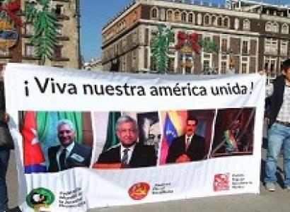People holding a big banner outside that says Viva nuestra america unida! and a lot of faces of people