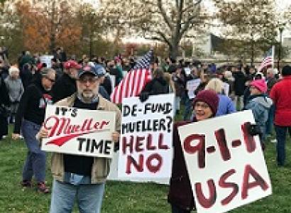 People outside gathered in a group holding signs that say It's Mueller Time, 9-1-1 USA