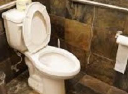 White toilet with lid up and toilet paper roll on hanger on wall under a silver bar against a brown tile wall and floor