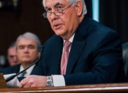 Older man with gray hair, a dark suit and pink tie sitting at a mic with glasses halfway down his nose