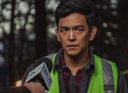 Man with dark hair and a yellow vest with a news media microphone aimed at him and he has a worried look on his face