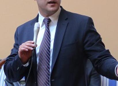Baldish white man wearing a suit holding a microphone and talking