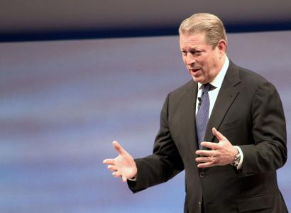 White man with graying dark hair in a suit holding his arms out in emphasis as he talks