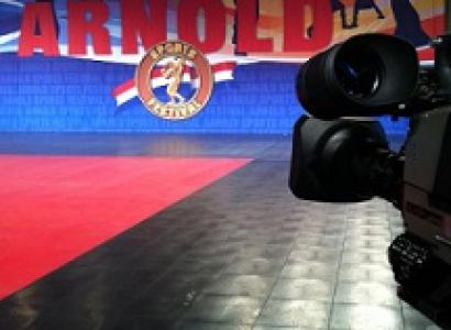 Closeup of back of a large videocamera shooting a large banner that says ARNOLD