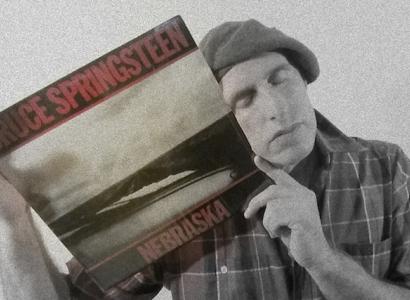 Guy wearing a beret with his eyes closed holding an album cover of Springsteen's Nebraska up to his face