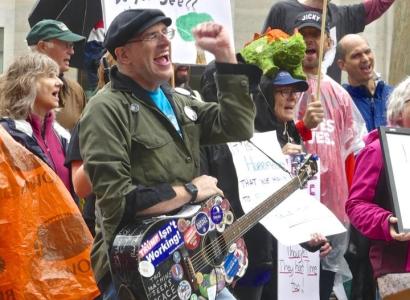 Guy with cap and guitar covered with stickers with his fist in the air in front of a crowd of people