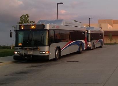 COTA bus, sllver bus with red white and blue curvy stripe on side driving in dusk