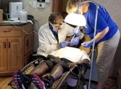Person in a dental chair and a dentist to the left working on them and a woman to the right, both with mask and gloves on
