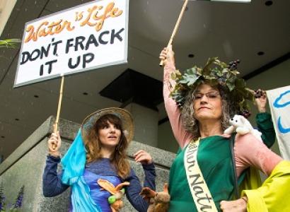 Two women dressed in gowns with protest signs saying Don't Frack it up and It's not nice to frack mother nature