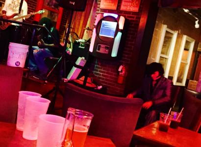 Sideways view of a bar with guy with guitar on stage lighting is very red