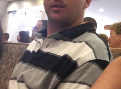 Man in his 20s with a bald head looking at the camera wearing a gray, white and black striped shirt