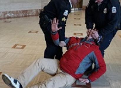 Man being dragged across the floor by two uniformed policemen