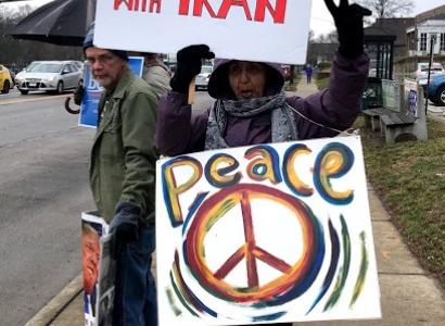 Woman holding No War with Iran and Peace protest signs