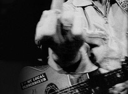 Guy making a mean face holding a guitar and giving us the middle finger