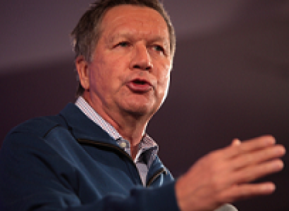 Older white man gesturing as he speaks holding a mic
