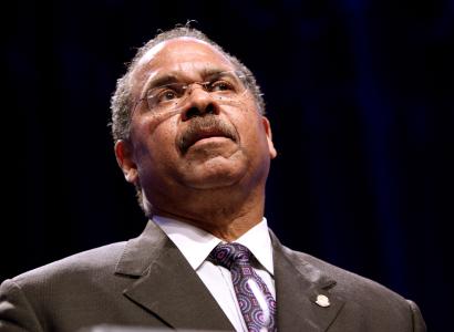 Black man in a suit with glasses speaking with his head tilted back