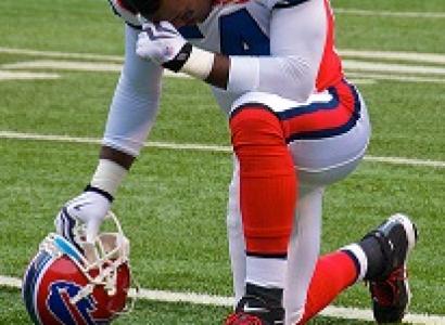 Football player wearing red white and blue football uniform kneeling on field