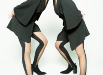 Two women with red hair and black outfits leaning towards each other