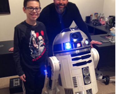 Man and young boy posing next to a robot that has a round top and white round body