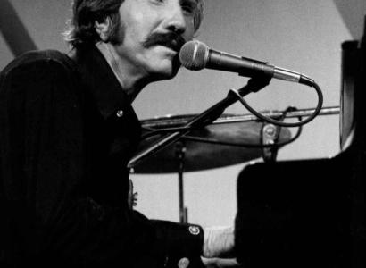 Black and white photo of guy with big mustache sitting at piano singing