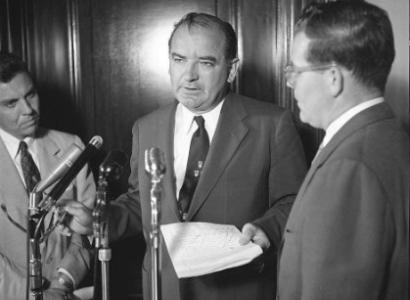 McCarthy talking at a microphone 