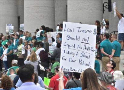 Person holding a sign against the Medicaid cuts at the statehouse with lots of other people