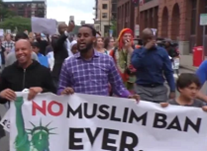 People marching outside with sign saying No Muslim Ban Even