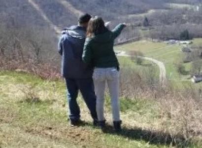 Backs of two people standing outside on a hill pointing off to the distance down in a valley
