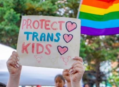 Someone holds aloft a sign reading "Protect trans kids." 