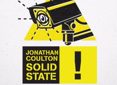 Yellow triangle with security camera with an eye on the screen above black words on yellow saying Jonathan Coulton Solid State excalamation point