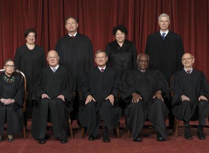 Photo of men and women posing and facing the camera all wearing long black robes in front of a dark red curtain