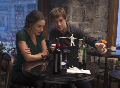 Man and woman sitting at a table looking at small replica of man on a wire between two towers