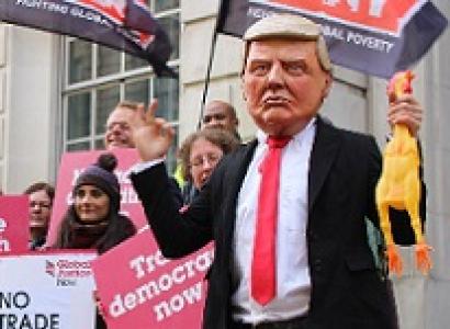 Man wearing Trump mask at demonstration with people holding signs saying No Trade Deal with Trump