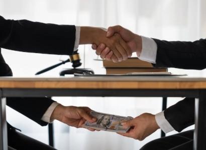 Two men shaking hands above the table and exchanging money under the table