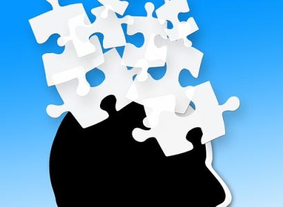 Black silhouette of a head facing right with white puzzle pieces flying out of his head against a blue background