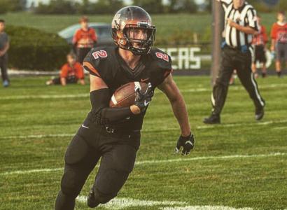 Football player running with the ball in his arm in brown and orange uniform