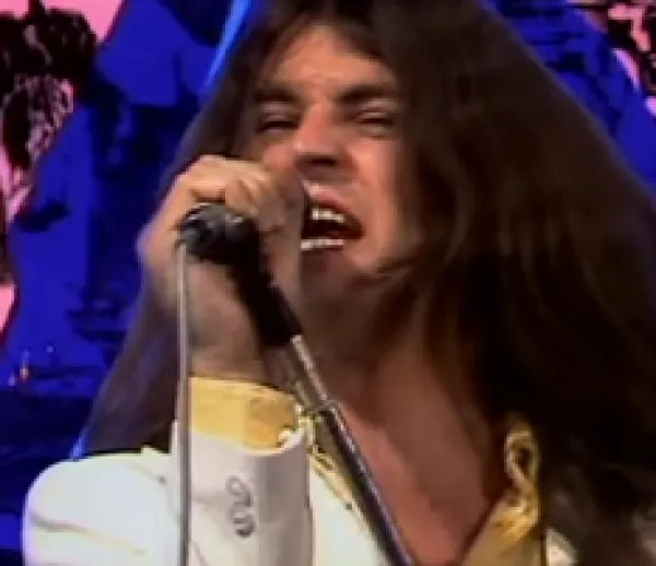 Long white man rock singer belting out a song into a mic with a blue and pink psychedelic background