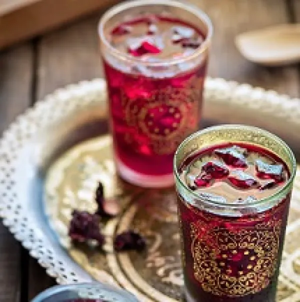 Two glasses with gold designs on the outside and red liquid inside on a pretty gold flouted tray against a wooden tabletop