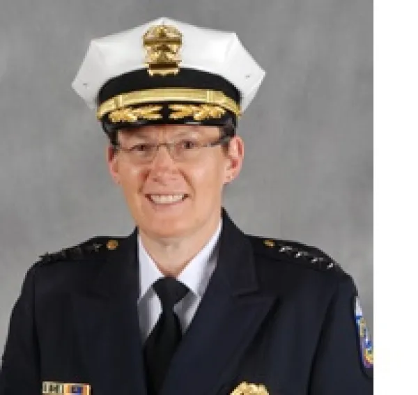 White woman in a police uniform and wire rimmed glasses smiling and posing