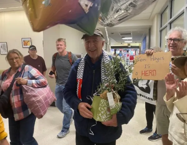 Man walking through airport holding a plant with people and balloons surrounding him