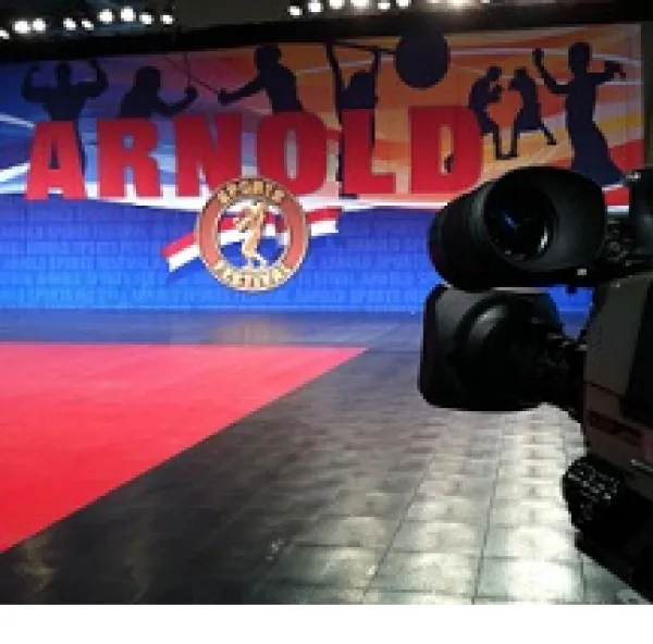 Closeup of back of a large videocamera shooting a large banner that says ARNOLD