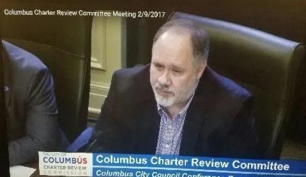 Bald man with gray goatee at a official city meeting
